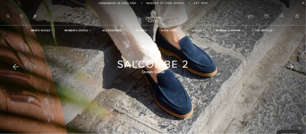 Luxury footwear brand website featuring blue suede loafers on stone steps with premium full-screen homepage design.